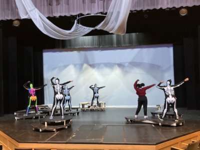 A group of students in costume and regular dress rehearse the skeleton dance