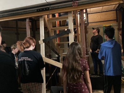 A group of rehearsing students looks up at a ladder leading to the the stage trapdoors.