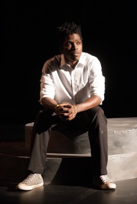 Male student performer sitting on stage wearing white shirt and black pants