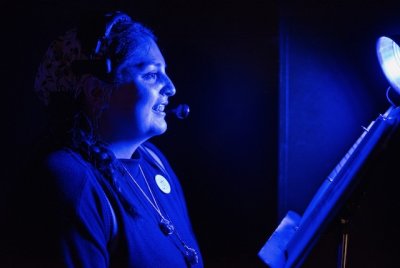 A student wearing a headset smiles looking toward the right. She is bathed in blue light.