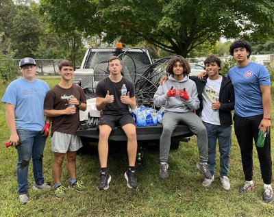 Team of male students sitting around the bed of a pickup truck, smiling for the camera.